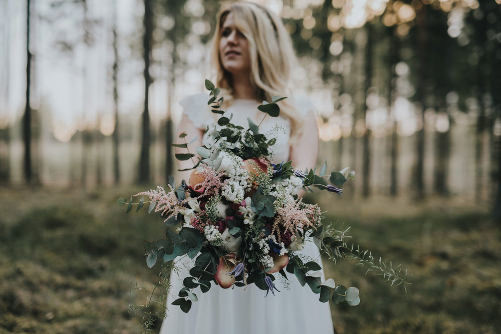 Brud med vild brudbukett i skogsmiljö under fotografering av bohemiskt bröllop i Halmstad