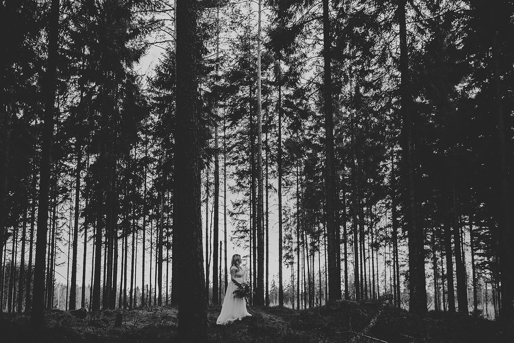 Brud med bröllopsklänning i spets och vild bukett i skogsmiljö