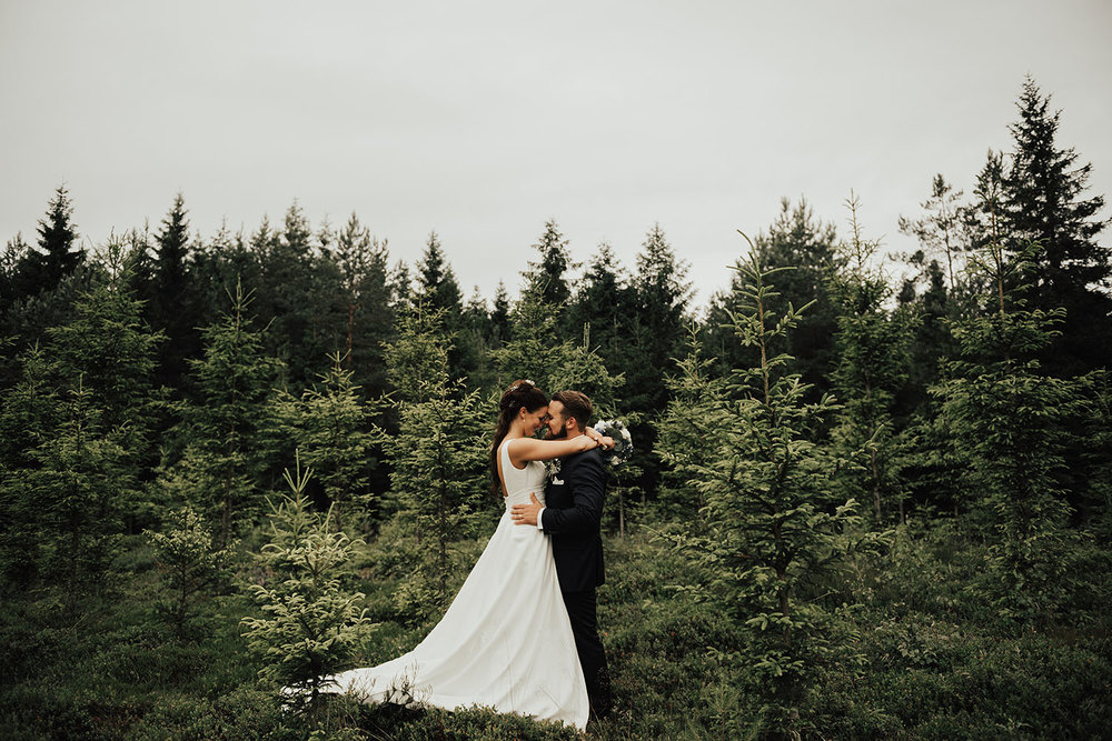 Brudpar under fotografering med bröllopsfotograf i granskog