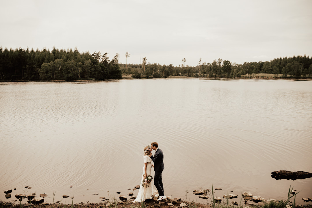 brudpar med bohemiskt midsommarbröllop står vid sjö