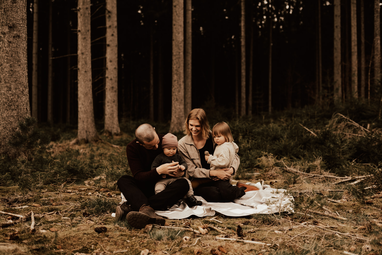 Familj sitter tillsammans på filt i skogen under fotografering