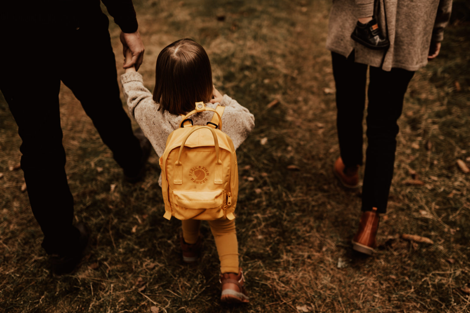 Barn med gul Fjällräven Kånken ryggsäck håller förälders hand under promenad i skogen