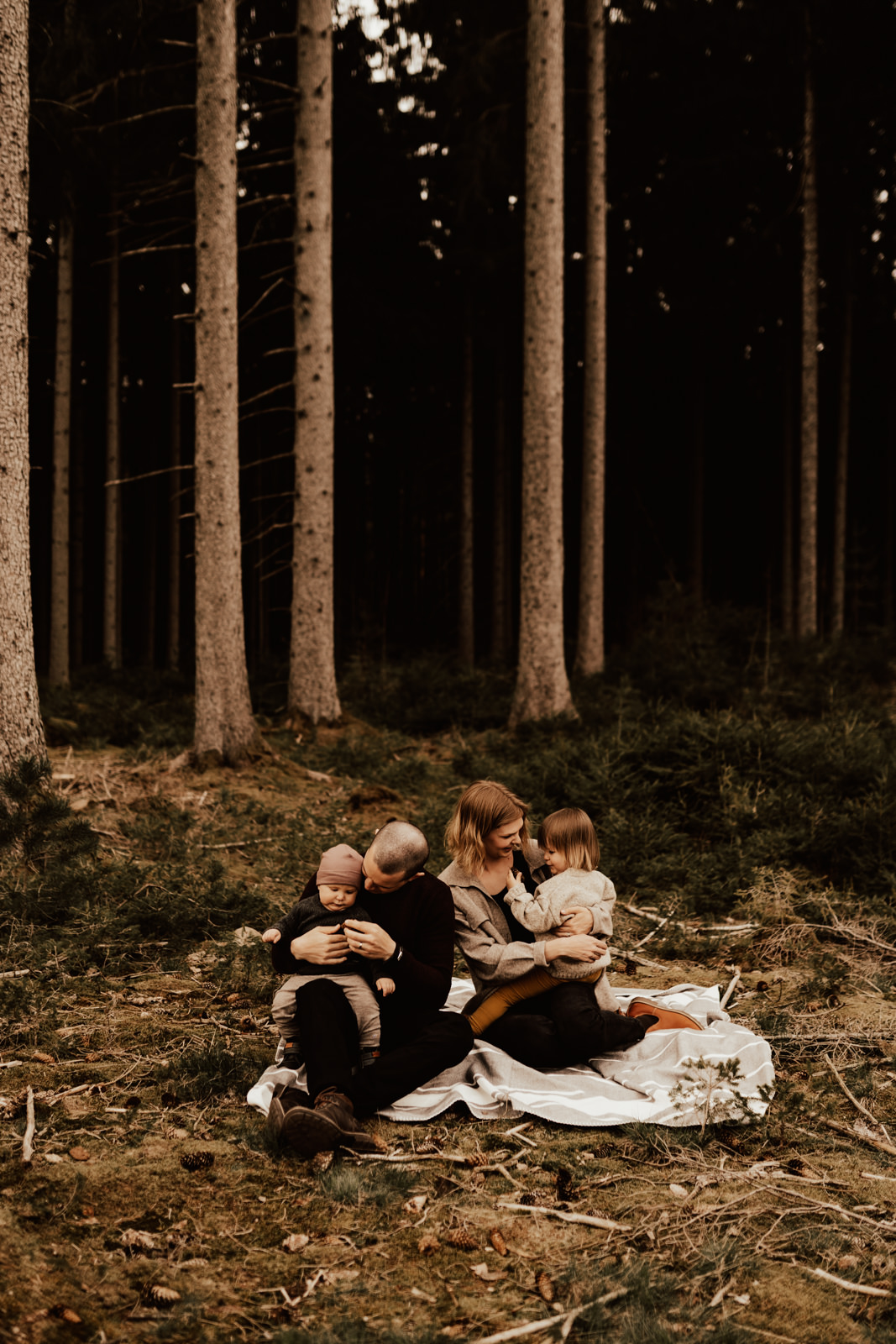 Familj sitter tillsammans på filt i skogen under fotografering