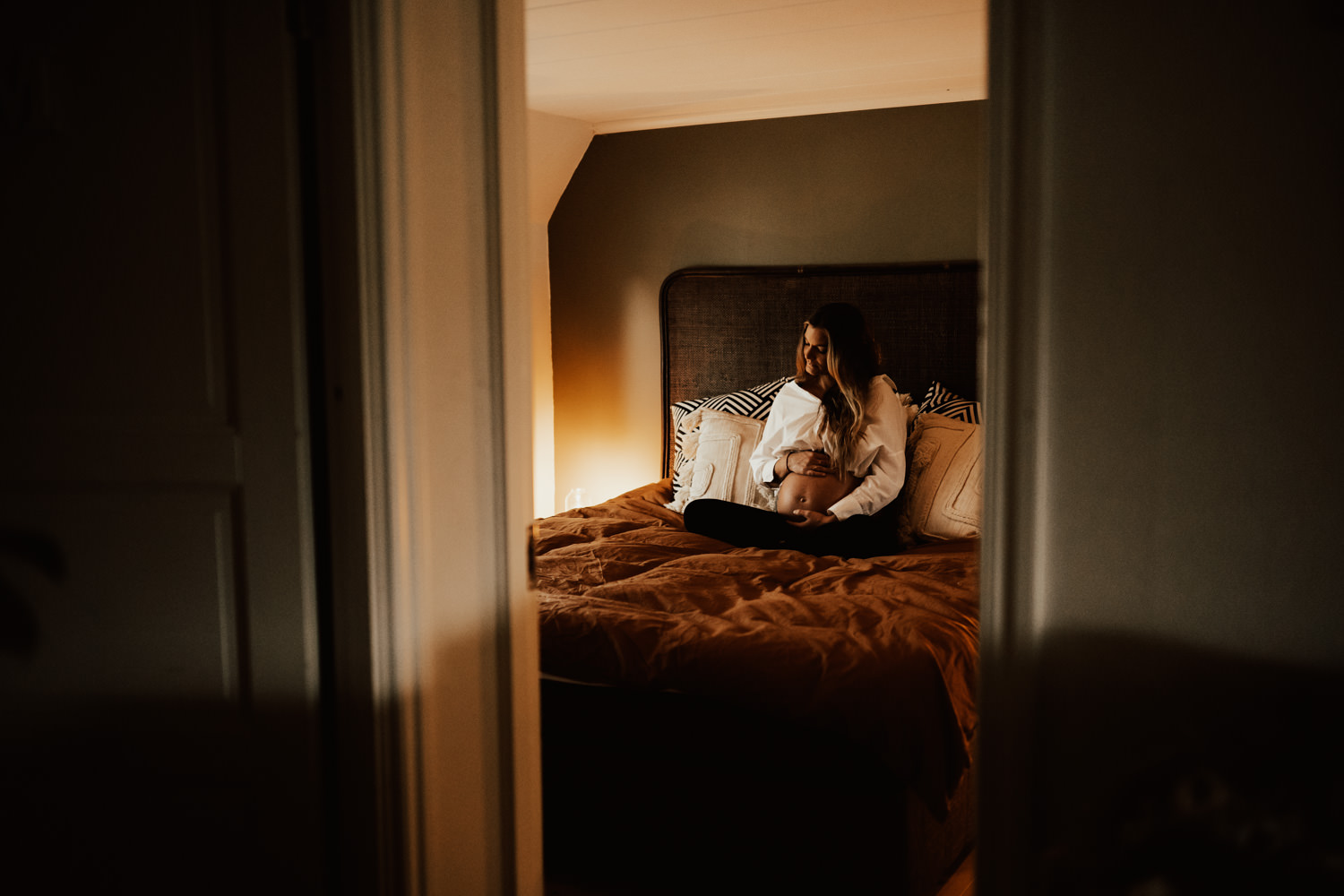 Gravid sitter på säng i sovrum under gravidfotografering hemma