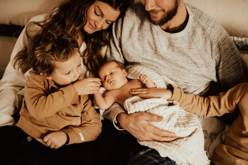 Familj kramas med nyfödd bebis i soffa
