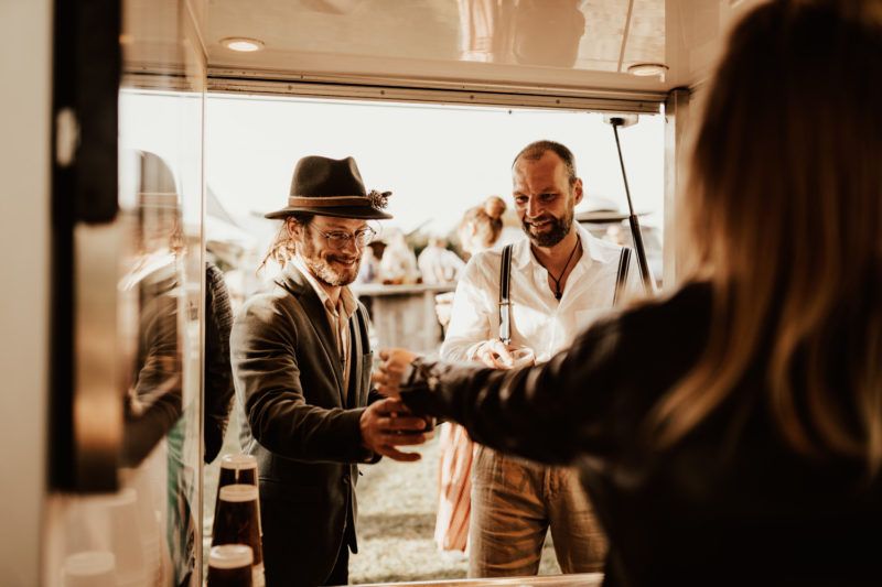 Groom and guest having beer at the beer truck at a boho festival wedding in Germany