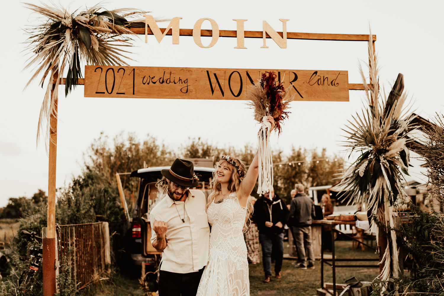 Couple standing and cheering in front of the entrance to their boho festival wedding in Germany
