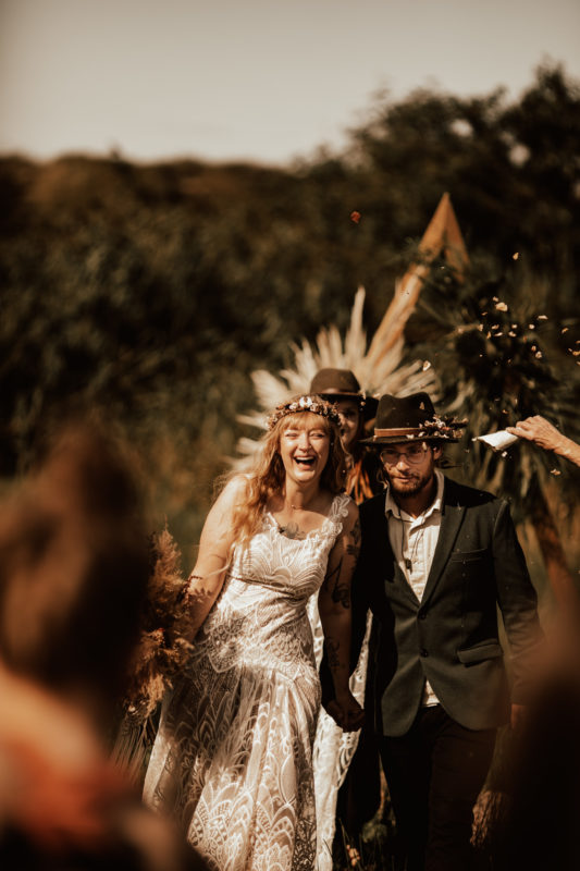 bohemian styled wedding couple laughs while turning to the guests during the ceremony in an outdoor wedding in germany