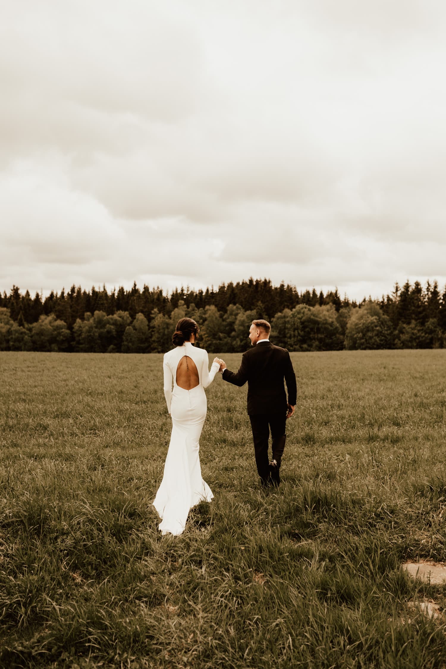brudpar går hand i hand mot skogen under bröllopsfotograferingen på Uddetorp Säteri