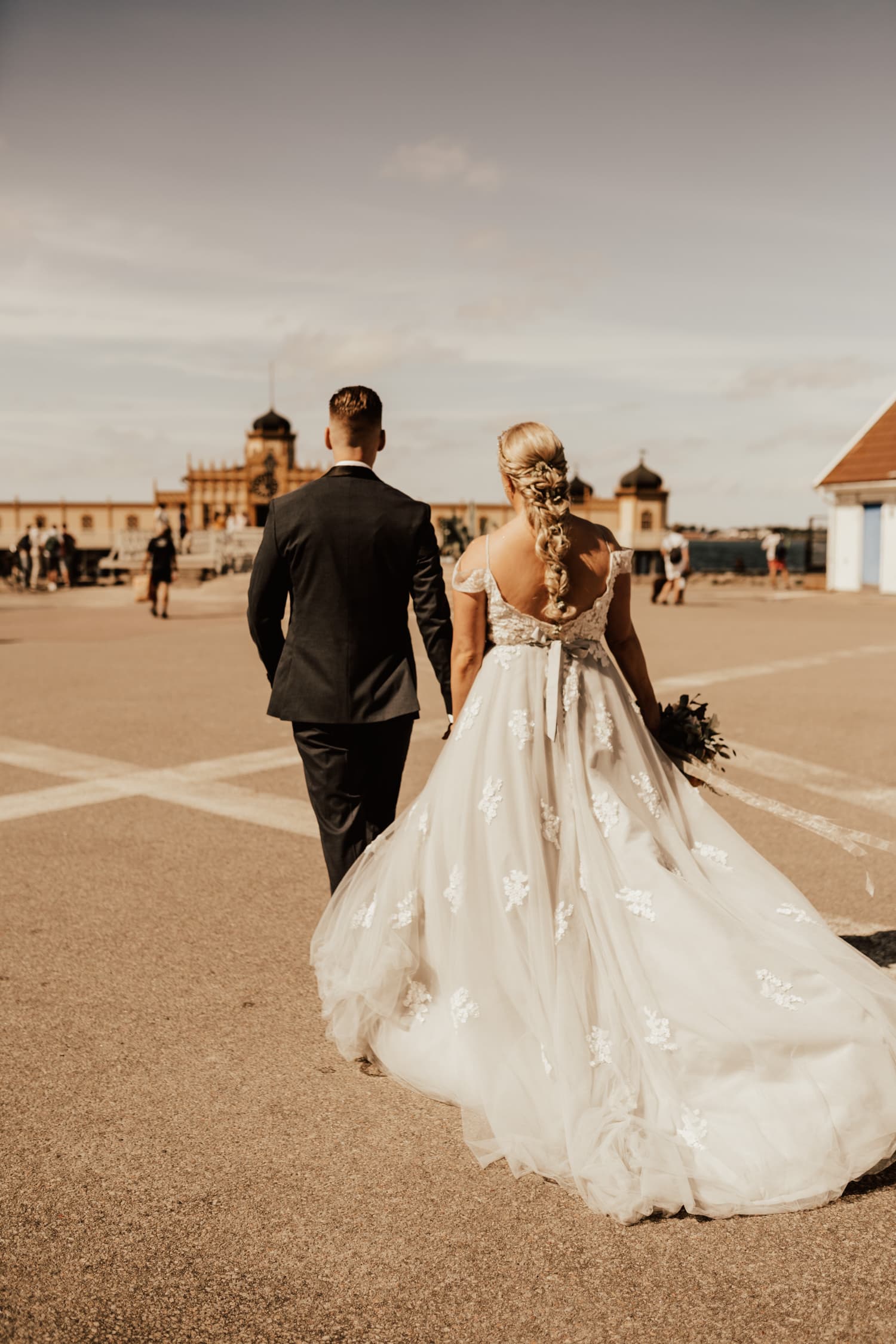brudpar går mot kallbadhuset i Varberg under deras bröllopsfotografering