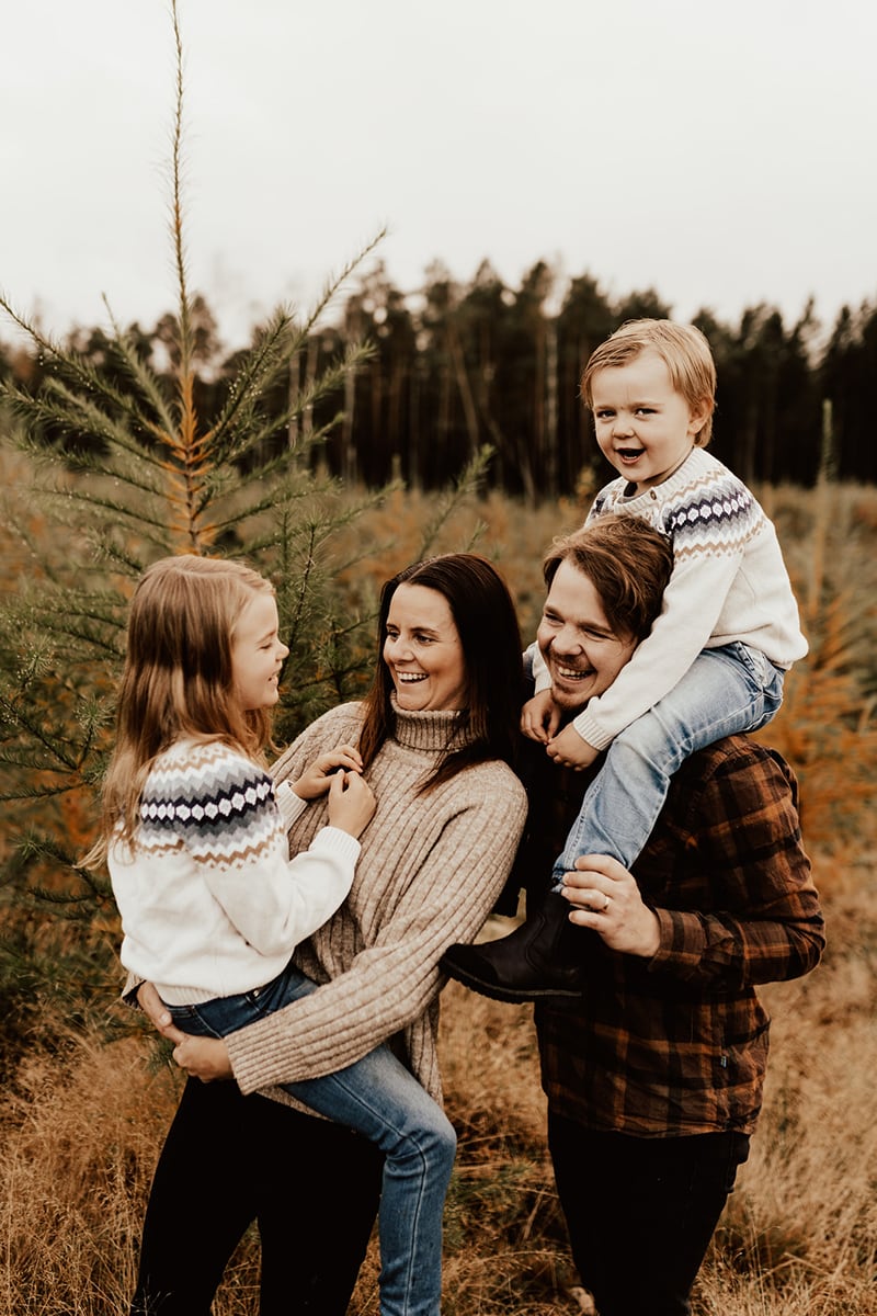 Föräldrar håller dotter i famnen och sonen på axlarna och skrattar under familjefotografering i skogen