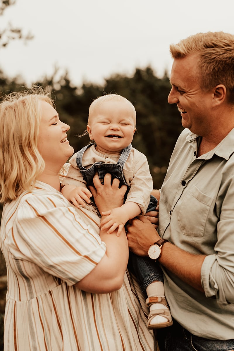Föräldrar håller i bebis som skrattar under familjefotografering i Halmstad