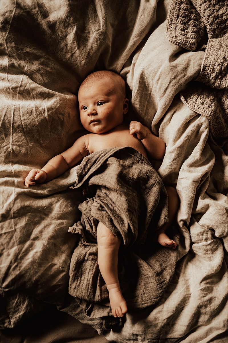 bebis ligger på lakan med filt i linne om sig