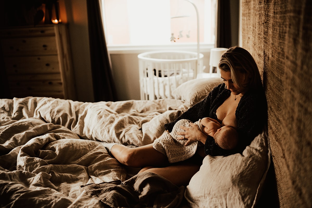 mamma lutar sig mot en bohemisk sänggavel och tittar ner mot sin bebis hon ammar