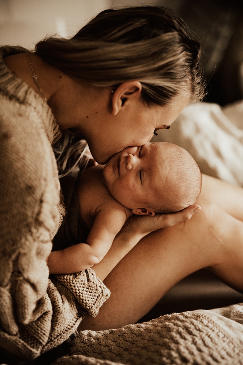 mamma sitter med bebis i knät och pussar den på kinden under fotografering i hemmet