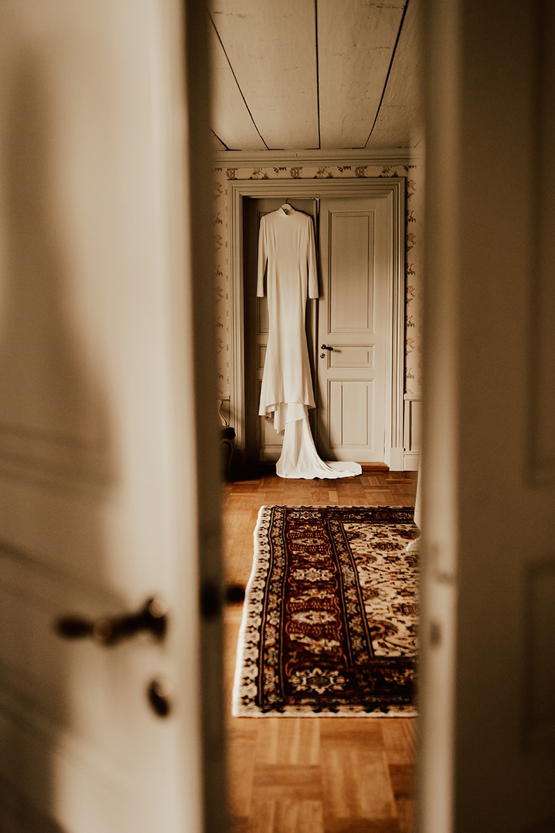 Stilren bröllopsklänning från Ida Lanto hänger på dörr på Uddetorp Säteri