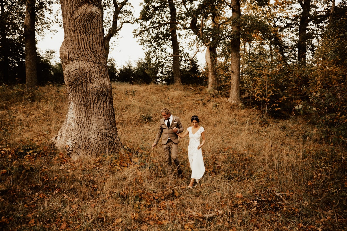 brudpar går ner för slänt i skogen under deras bröllopsfotografering på hösten