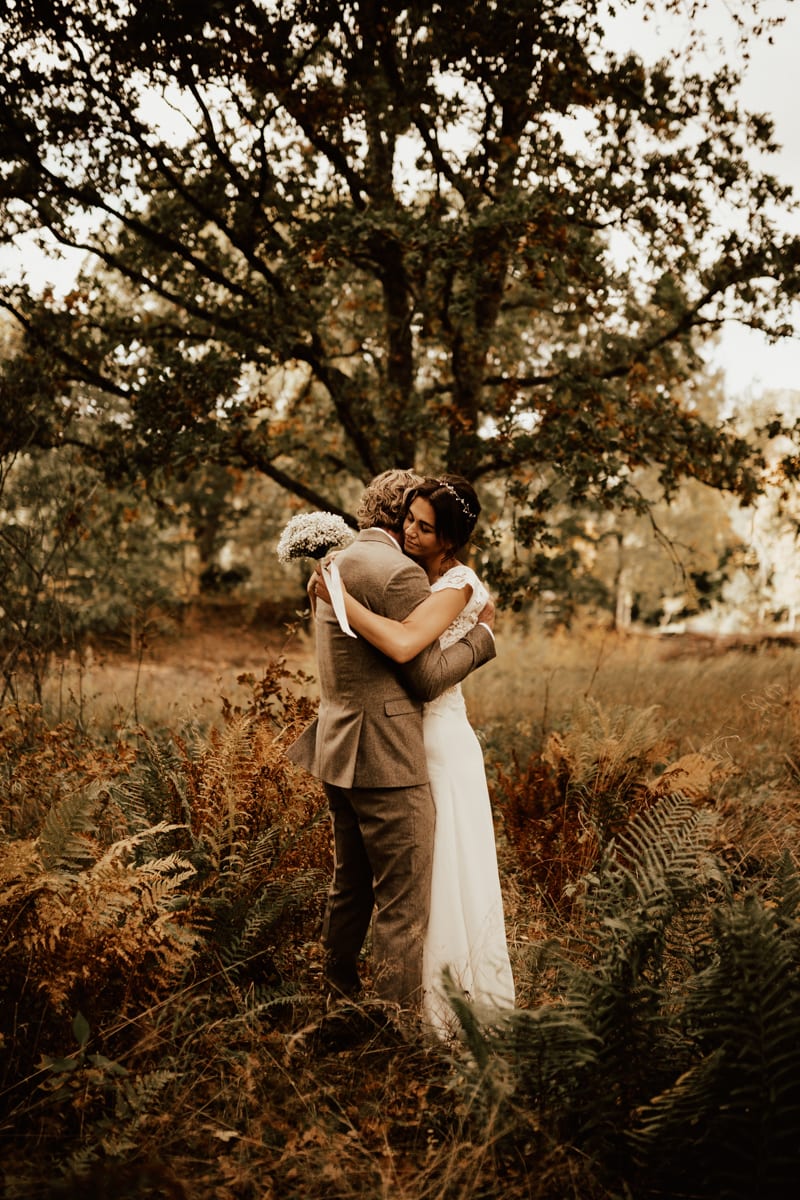 Brudpar står och kramas i skogen under deras höstbröllop i Sperlingsholm