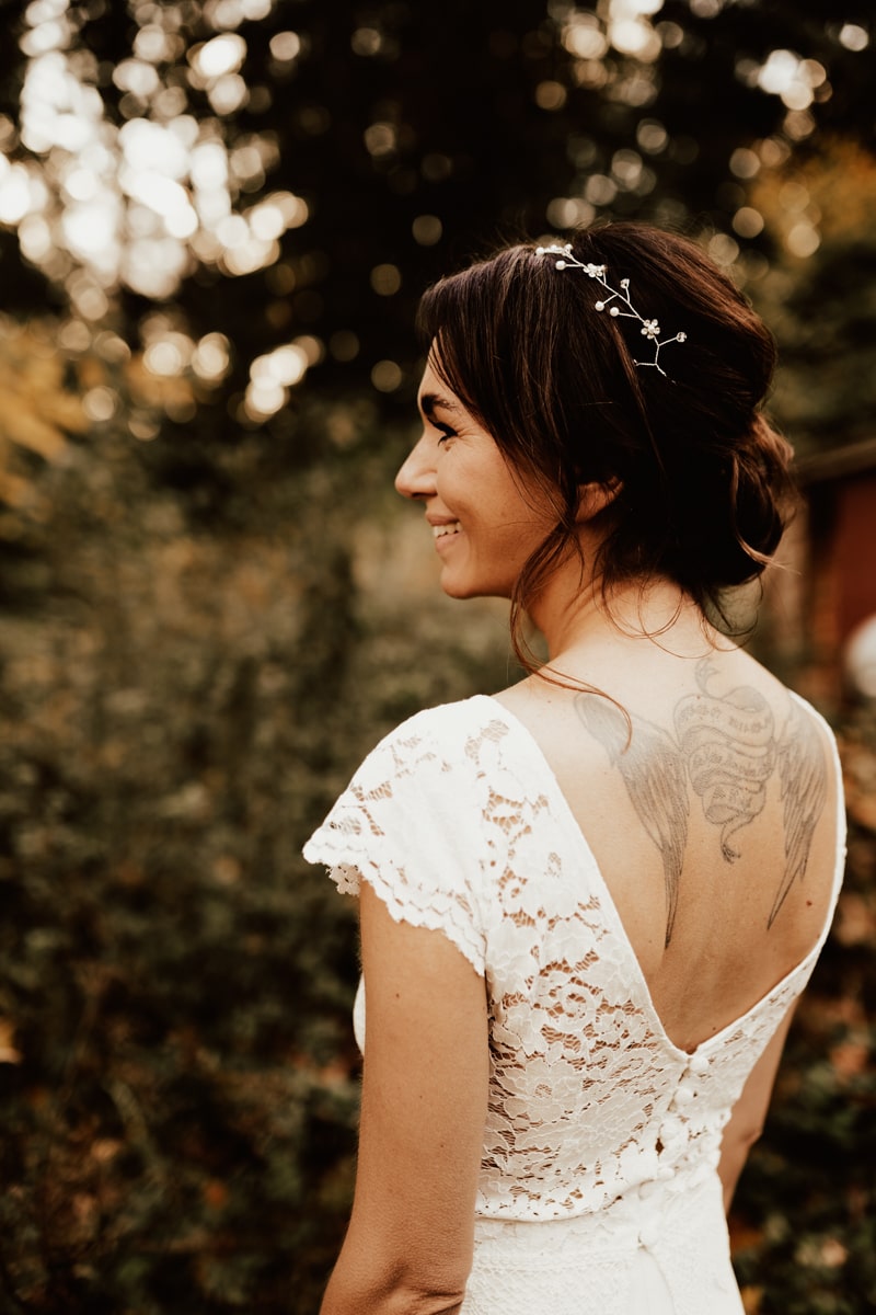 Brud i bröllopsklänning i spets med hårsmycke ler under höstbröllop i halmstad