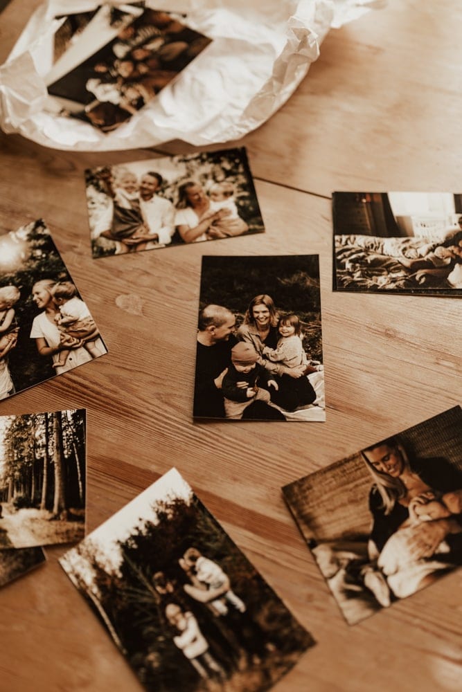 Utskrivna fotografier från familjefotograferingar i 10x15 ligger utspritt på en träbord.