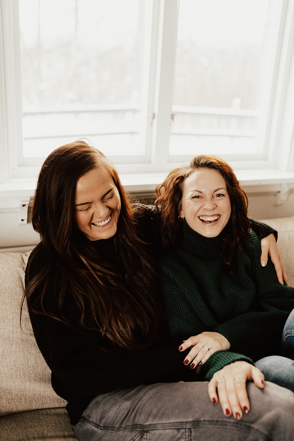två kvinnor sitter nära varandra i beige soffa och skrattar.