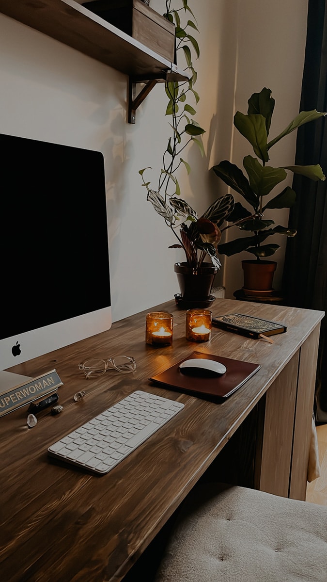 Egenbyggt betsat skrivbord på hemmakontor med iMac, växter och tända ljus.