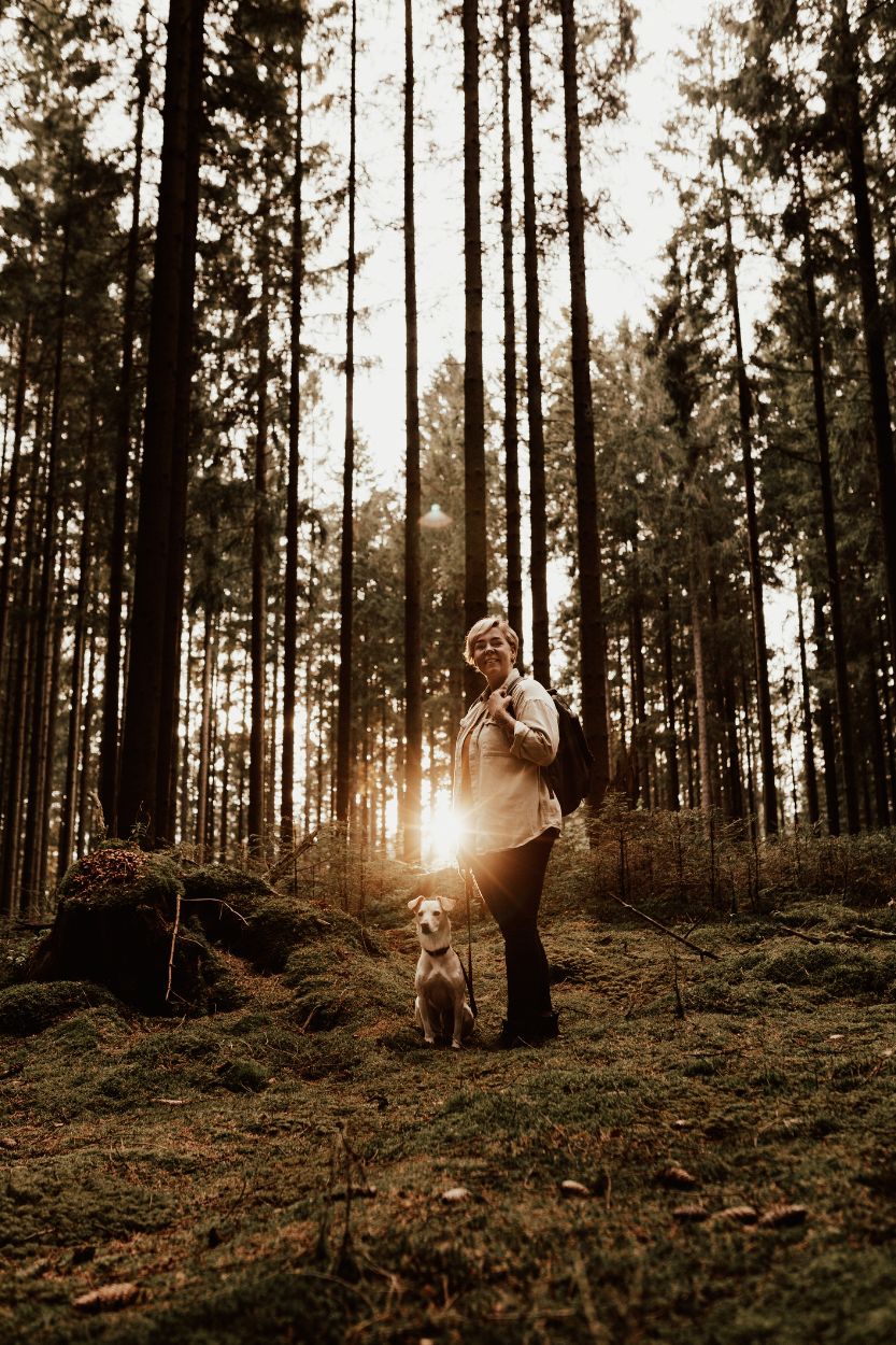Fotograf Linnsej Photography står i skogen med sin hund i solnedgången.