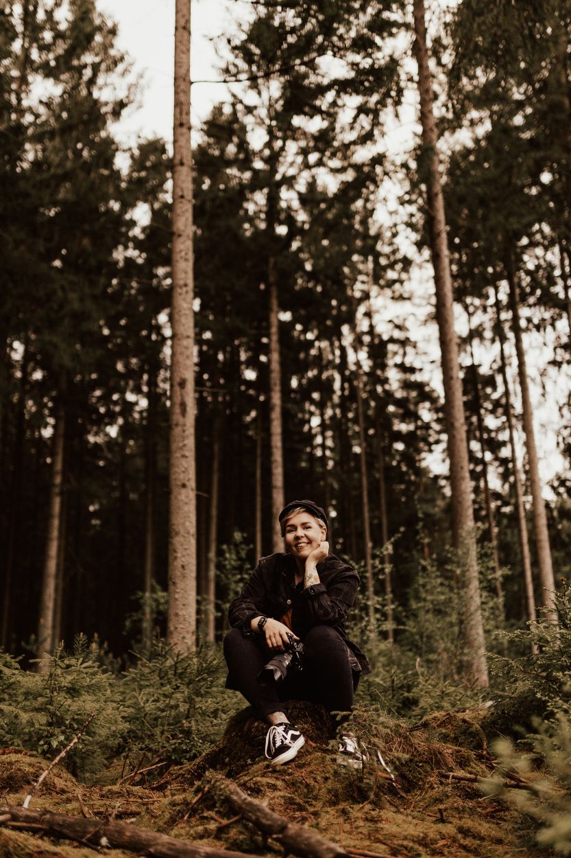 Fotografen Linnsej Photography sitter i skogen med sin kamera och ler.