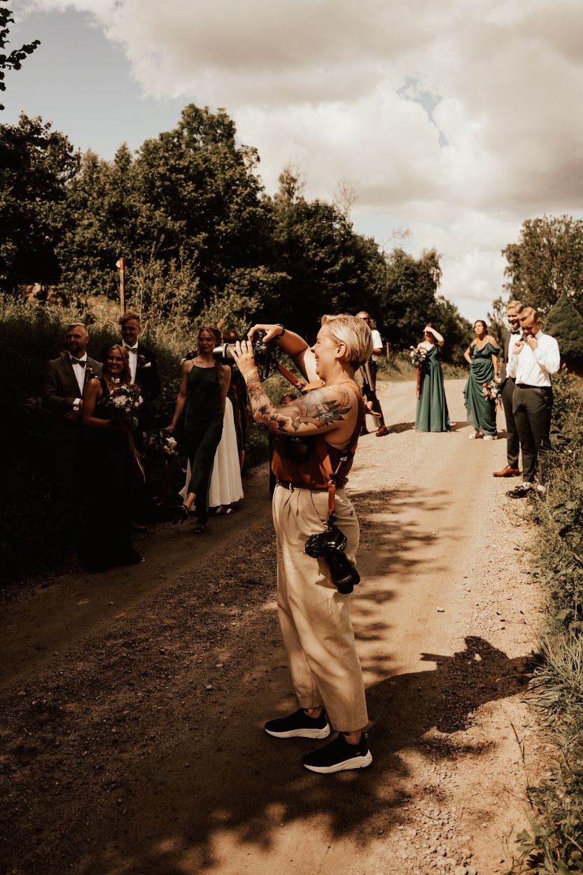 Bröllopsfotograf fotograferar brudfölje i skuggan en solig sommardag.